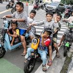 Sejumlah anak-anak menggunakan sepeda listrik di jalan raya.