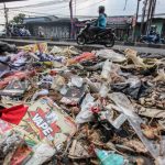 Pengendara melintasi tumpukan sampah yang menumpuk di pinggir jalan raya (1)