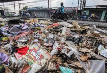 Pengendara melintasi tumpukan sampah yang menumpuk di pinggir jalan raya (1)