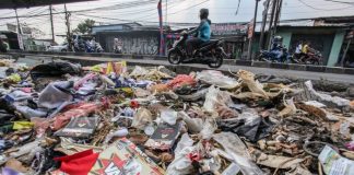 Pengendara melintasi tumpukan sampah yang menumpuk di pinggir jalan raya (1)